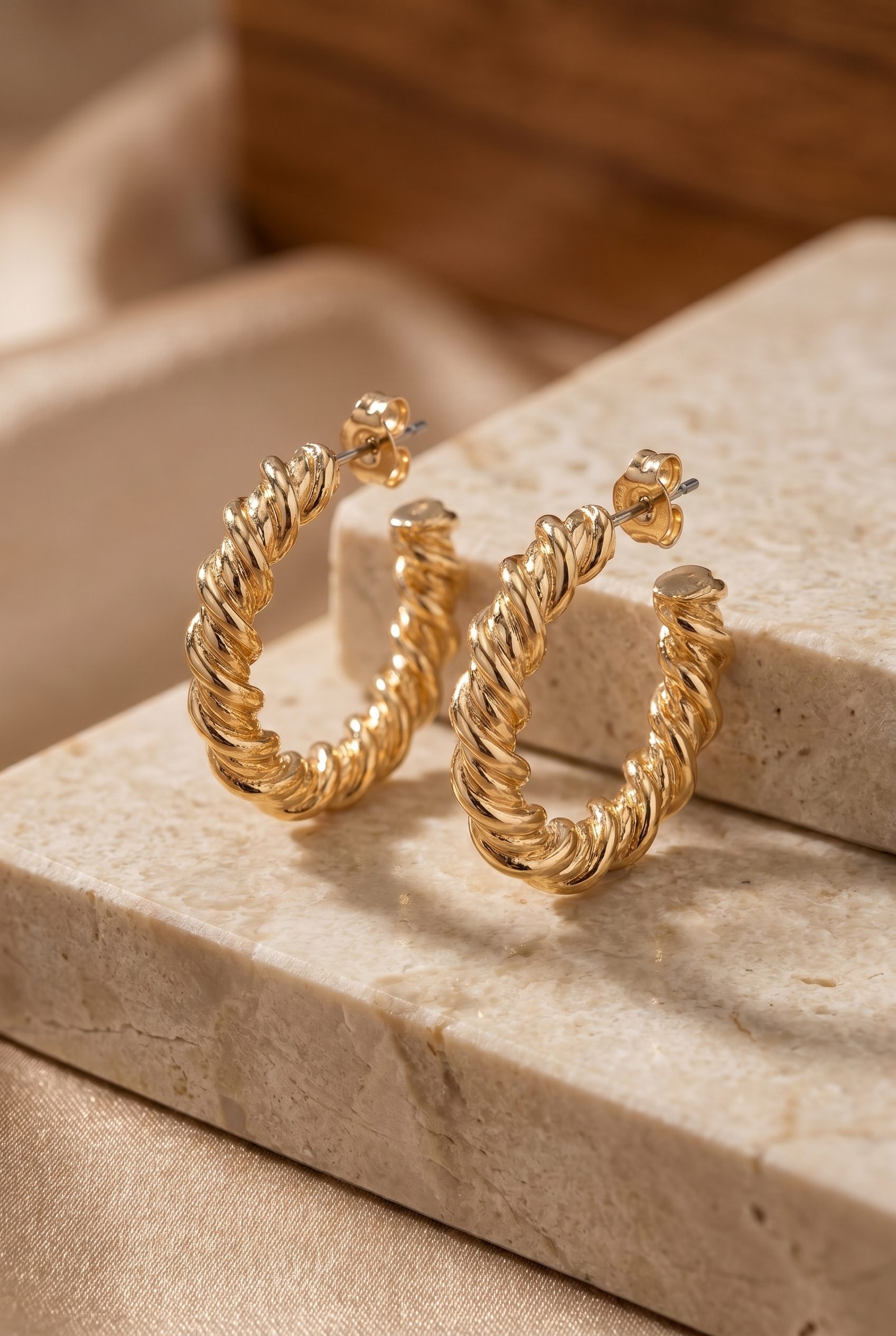 Fotogenic AI generated ecommerce accessories image of gold twisted hoop earrings on a polished marble surface