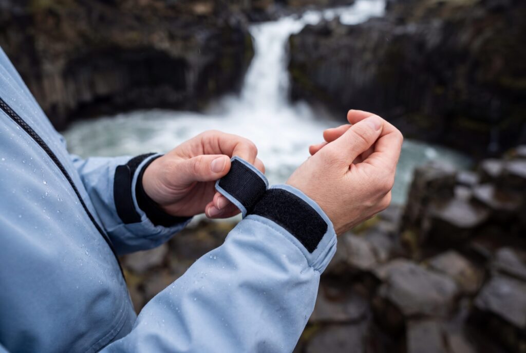 Close view of hands adjusting the cuff of a pale blue outdoor jacket.