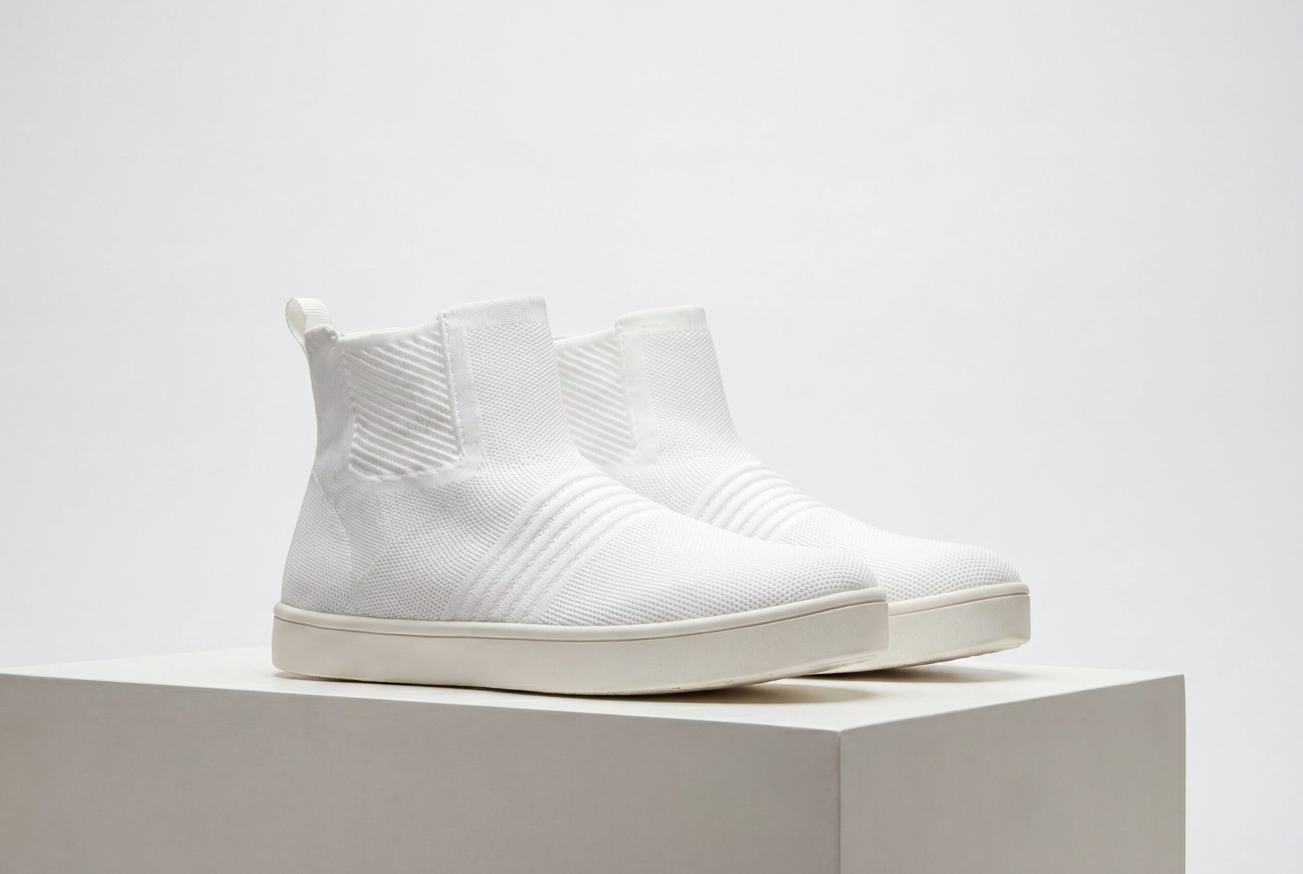 Footwear product photography audience image with blank-label white knit shoes on a studio plinth