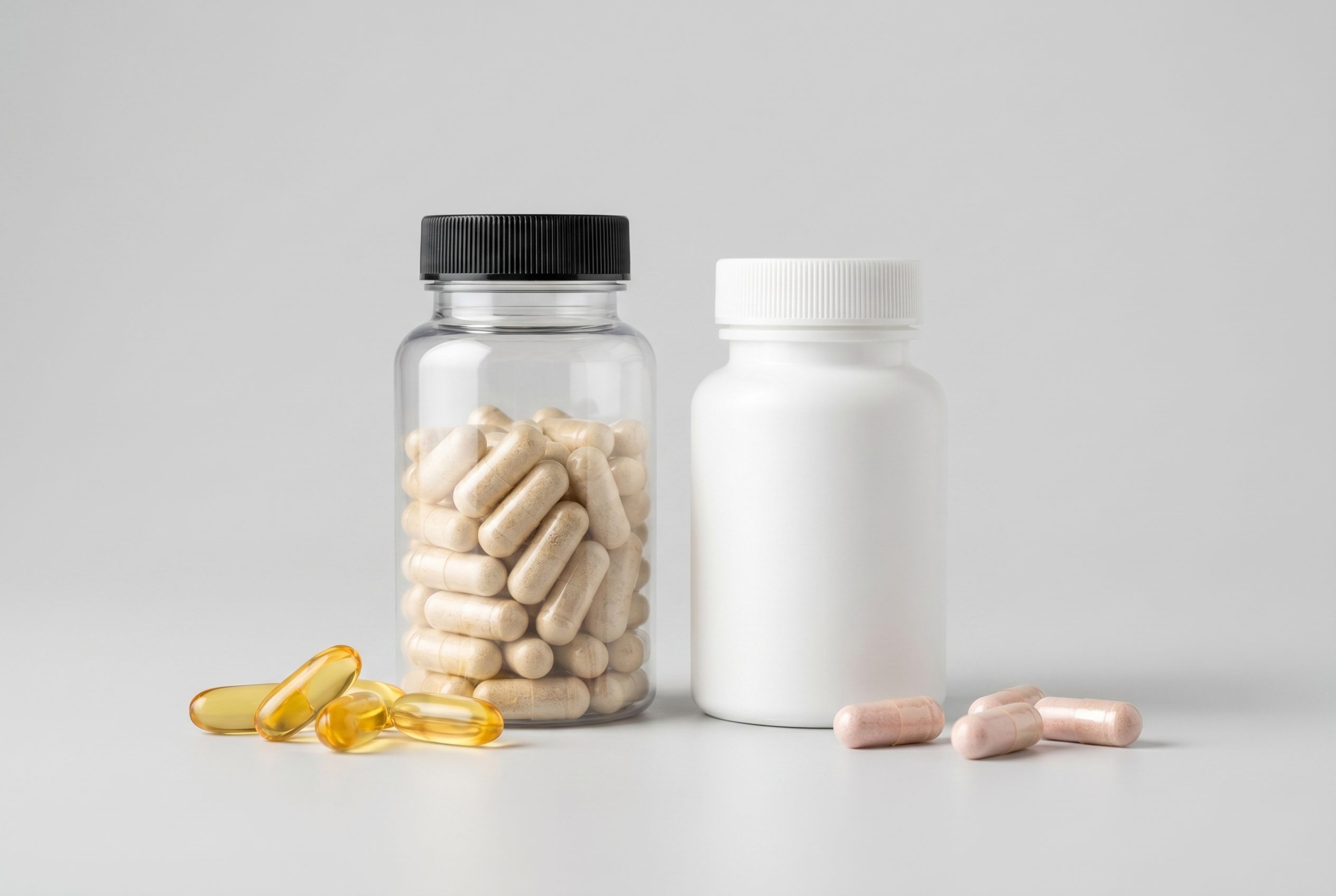 Brand-free capsule bottles with softgels and capsules on a clean neutral catalog surface.
