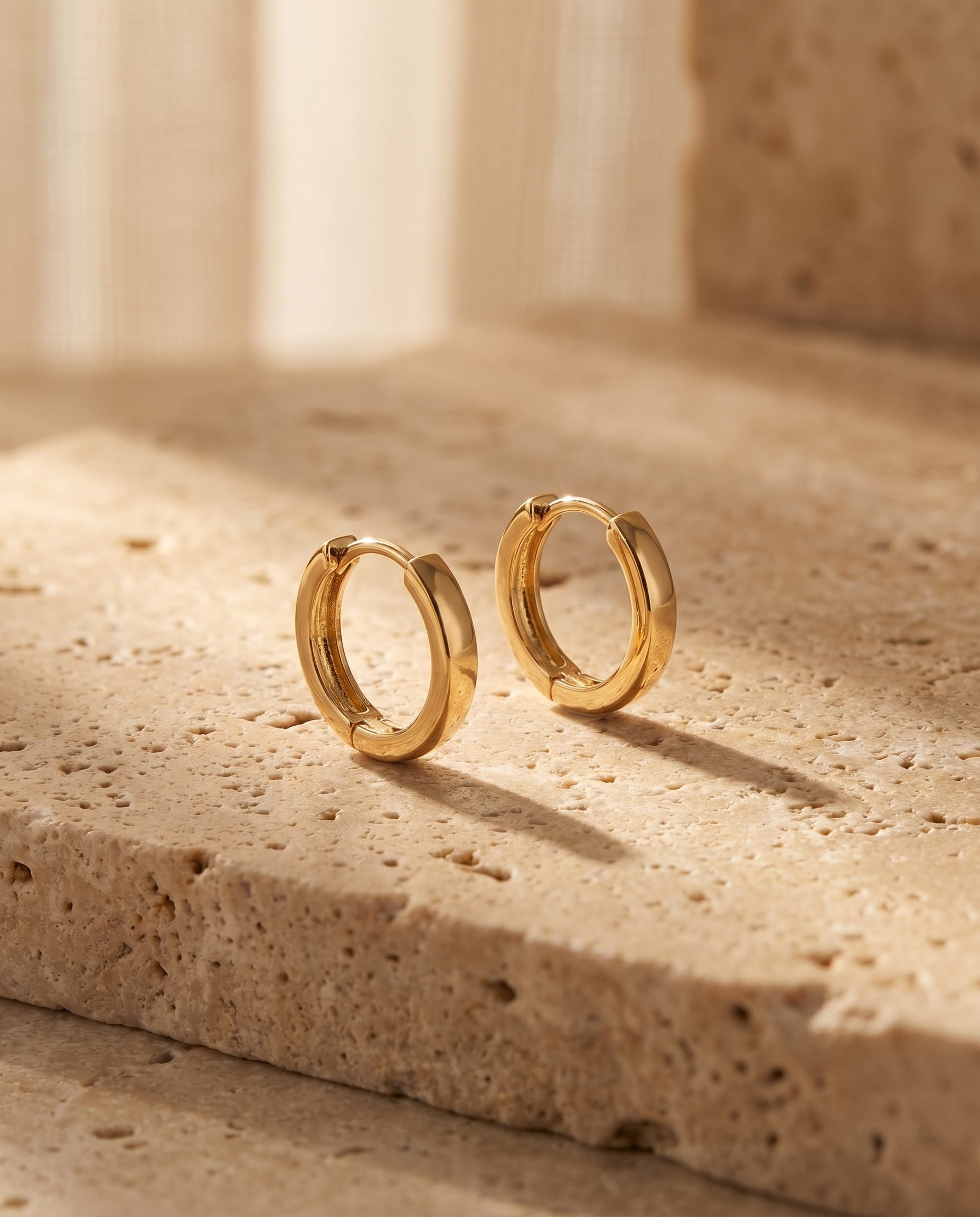 Gold hoop earrings styled as a warm product hero on textured stone.