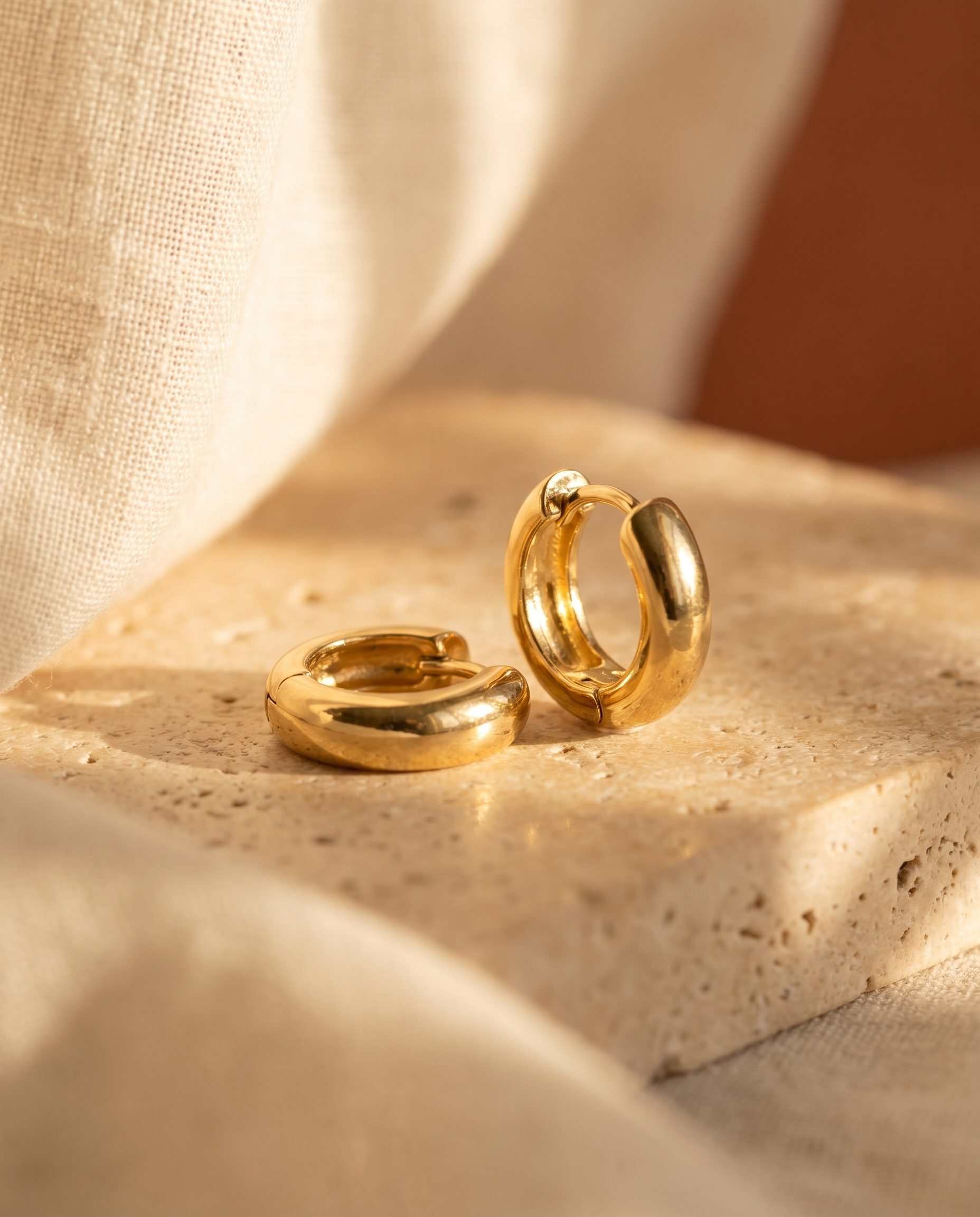 Gold hoop earrings shown in warm product detail light on textured stone.