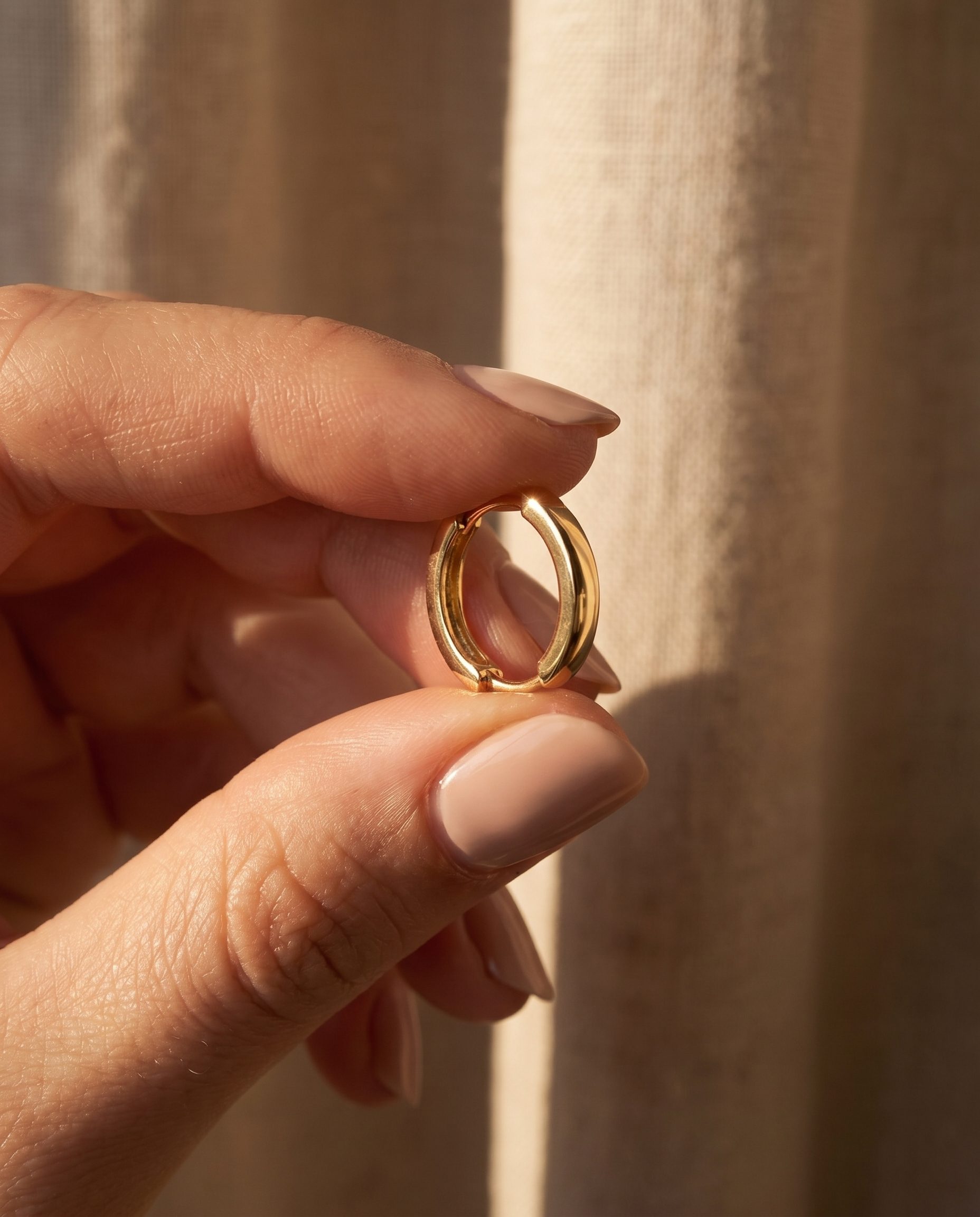 Gold hoop earring held in a warm close-up product detail campaign frame.