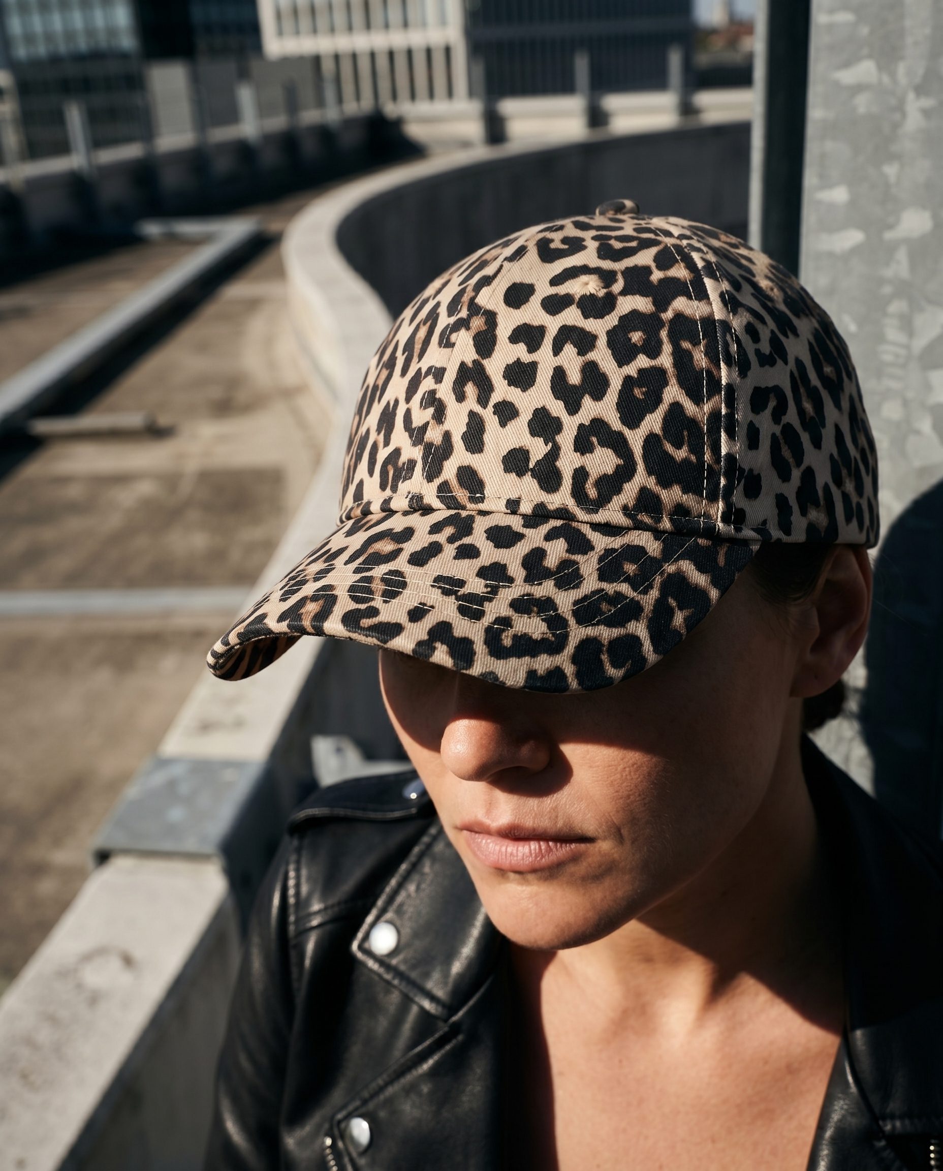 Leopard print cap worn by a model in a close rooftop fashion portrait.