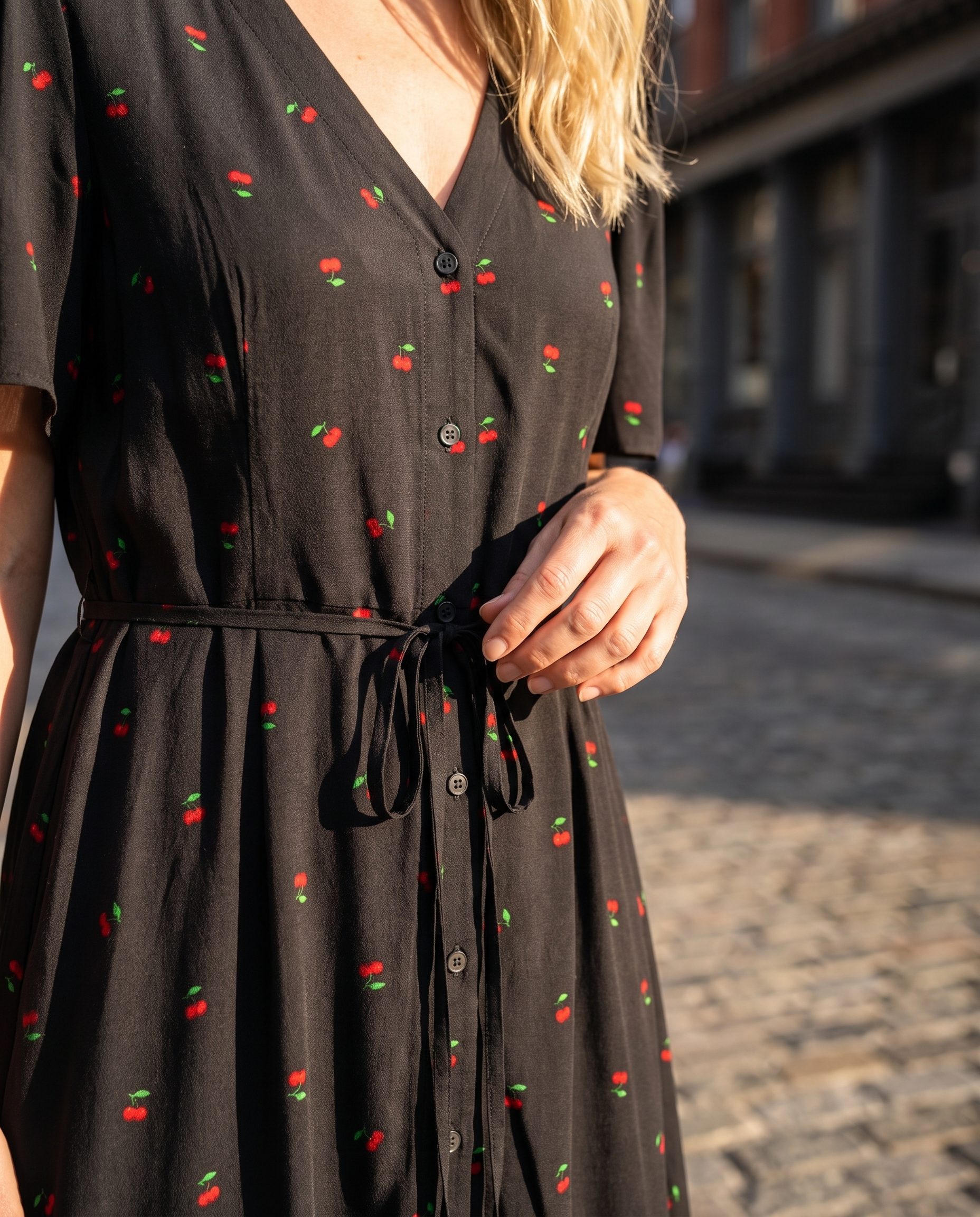 Close detail of a black cherry print dress with waist styling and fabric texture.