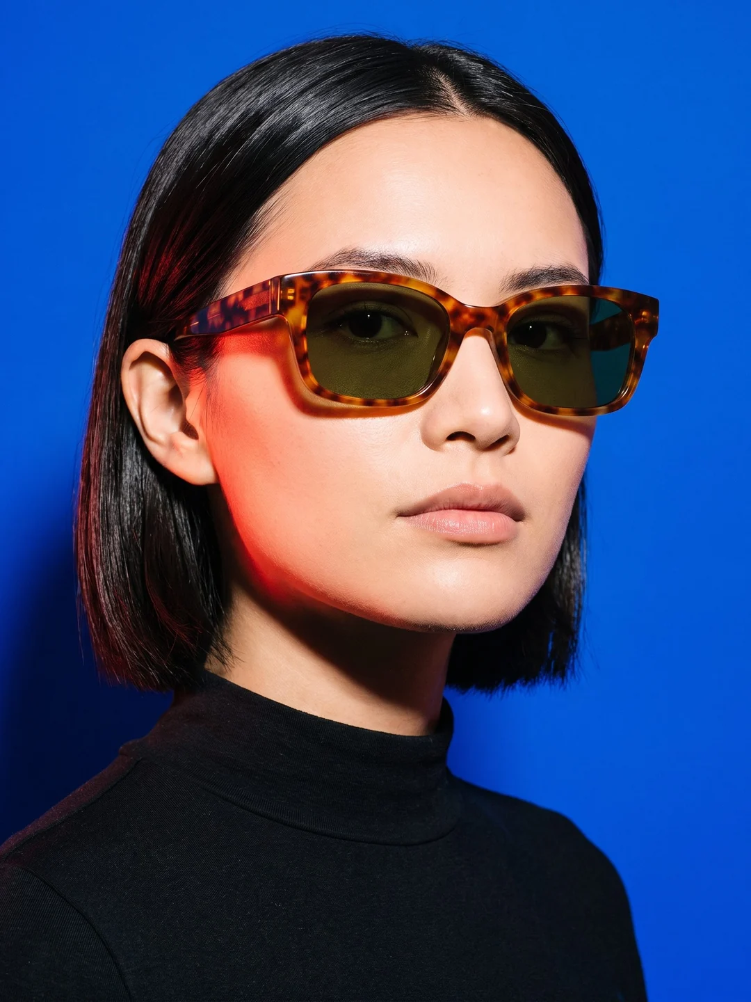 Adult woman wearing tortoiseshell sunglasses against cobalt blue