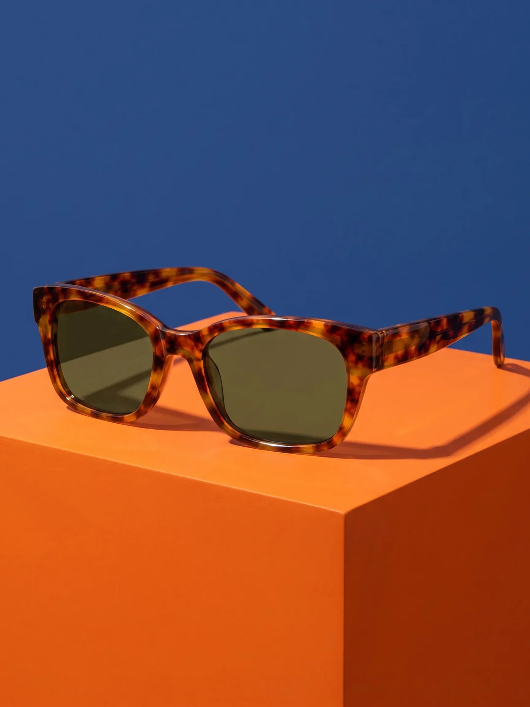 Tortoiseshell sunglasses on an orange plinth against blue