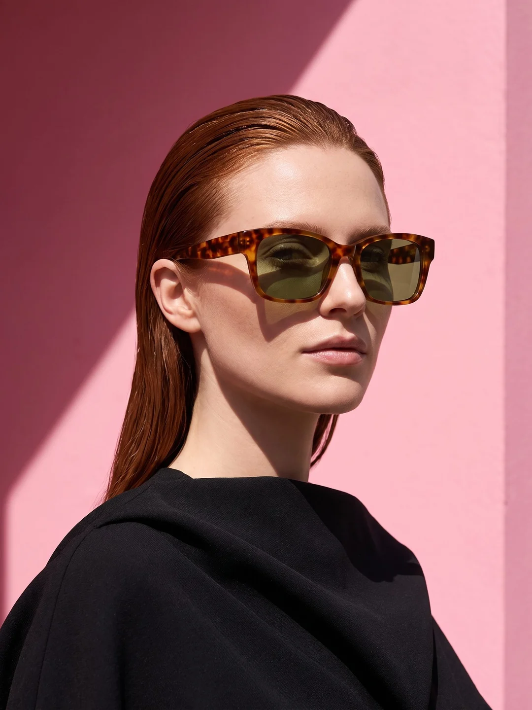 Adult woman wearing tortoiseshell sunglasses against a pink wall