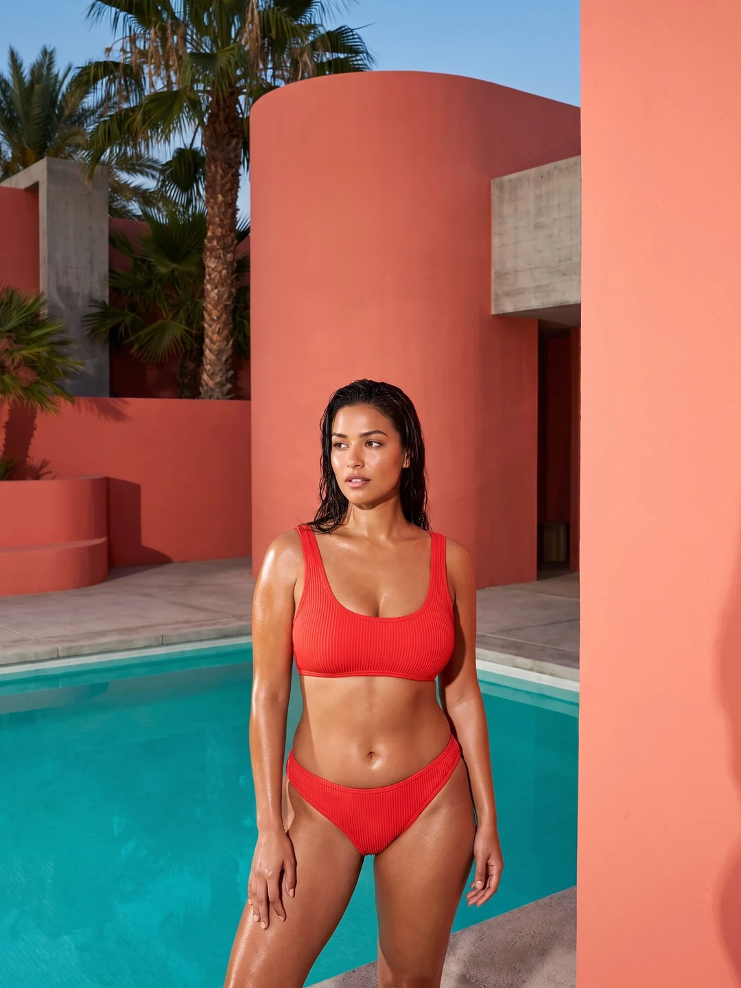 Adult woman wearing a coral bikini by a turquoise pool and coral architecture