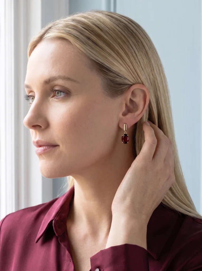 Closer worn view of the gold stud, connecting ring and garnet drop with hair held aside.