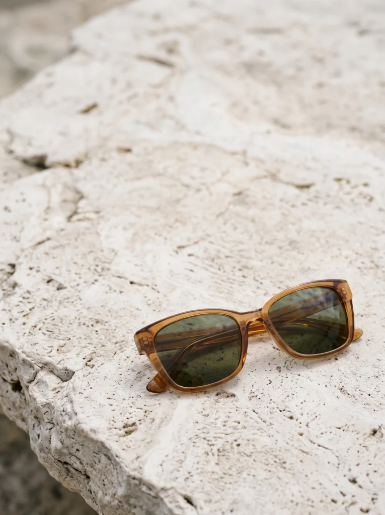 Folded amber sunglasses sit low in a composition of textured pale stone with open space above.