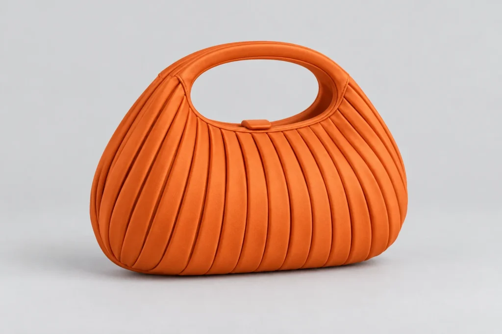 Orange pleated clutch concept reference with an integrated oval handle