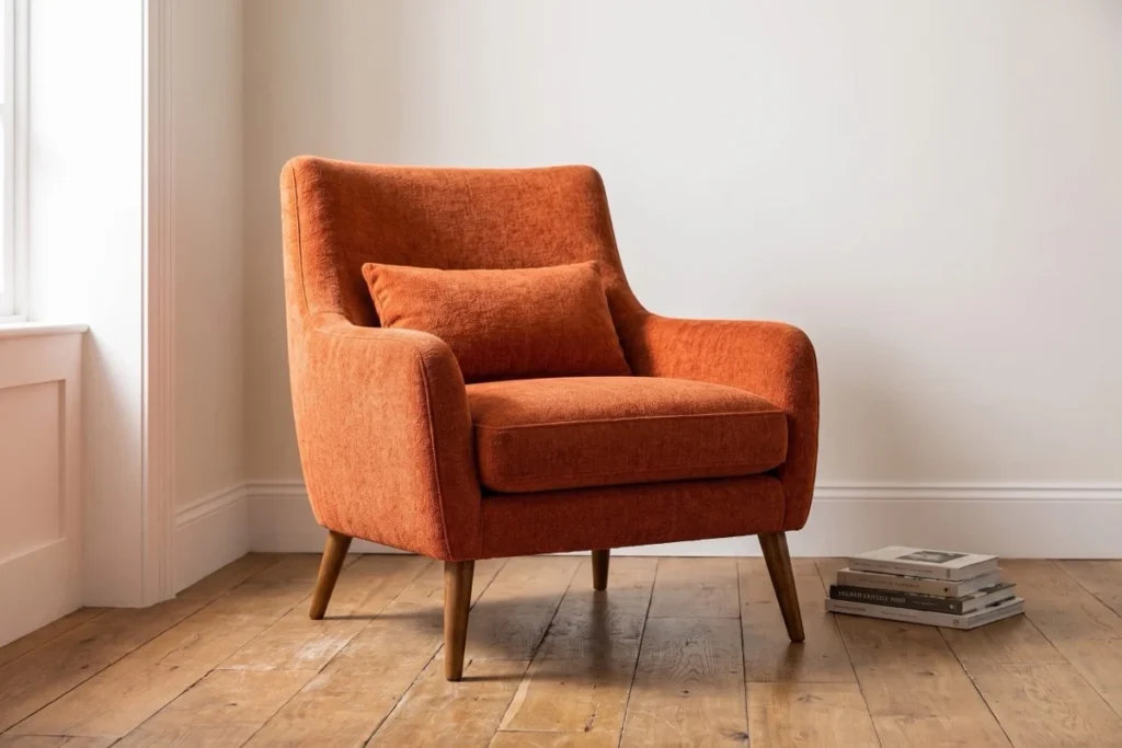 Rust upholstered armchair with wooden legs in a pale apartment reading corner.