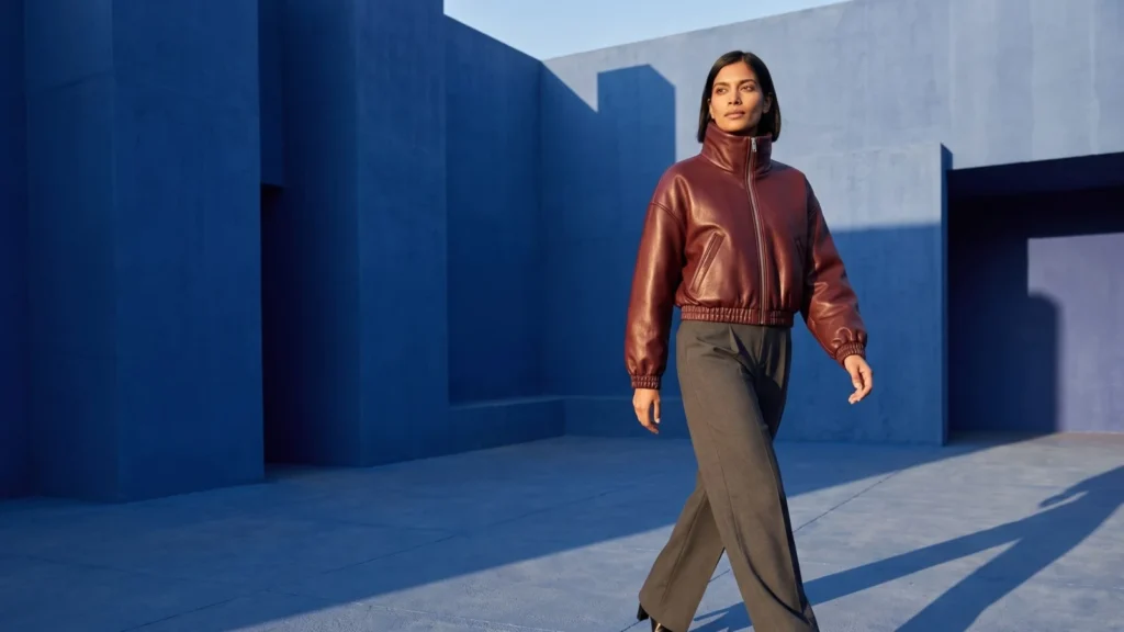 Dark-haired model wearing an oxblood bomber and graphite trousers in a cobalt architectural courtyard.