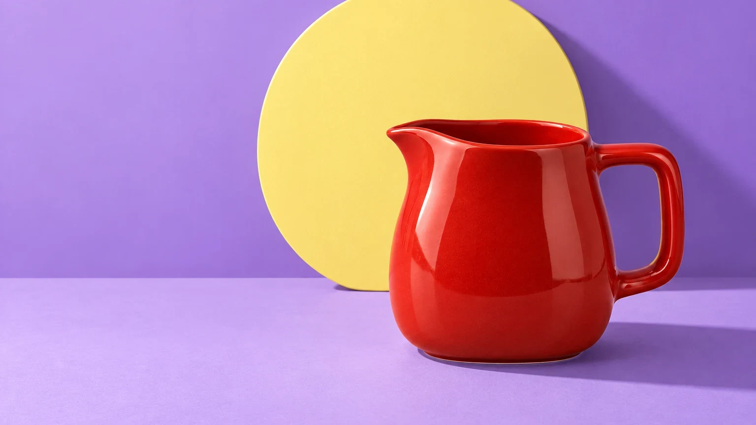 Red ceramic pitcher with a yellow disc against lilac