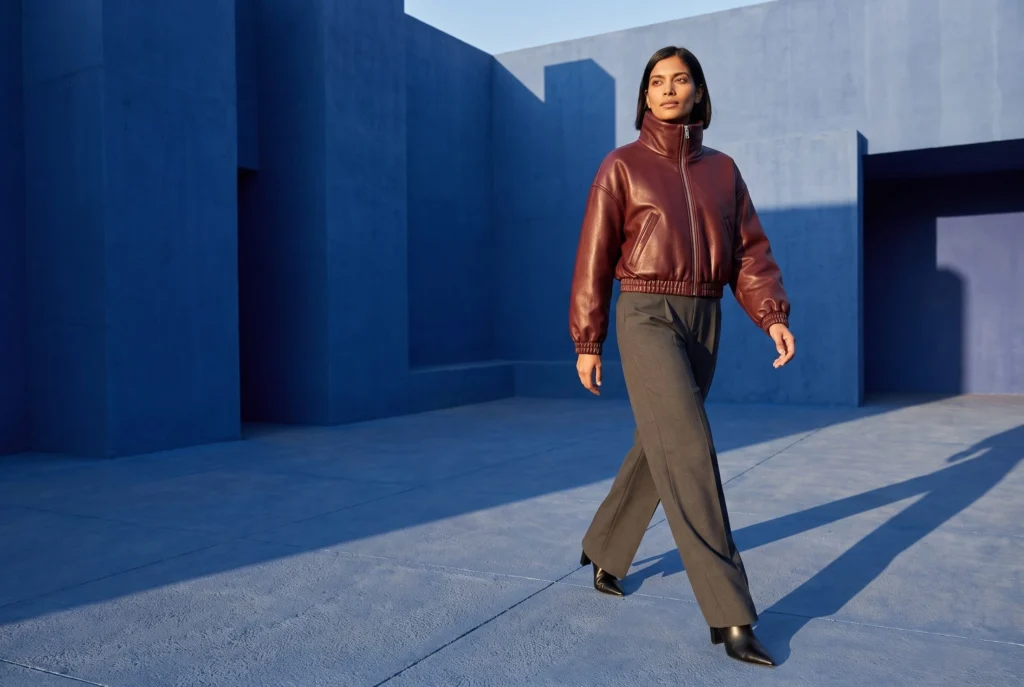 Woman wearing a burgundy leather jacket beside a cobalt-blue building.